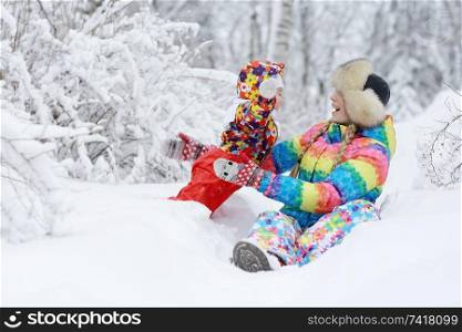 Daughter and mother are playing and lying in the snow in winter outdoors