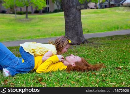 Daughter and mother playing lying on park lawn outdoor dressed in yellow