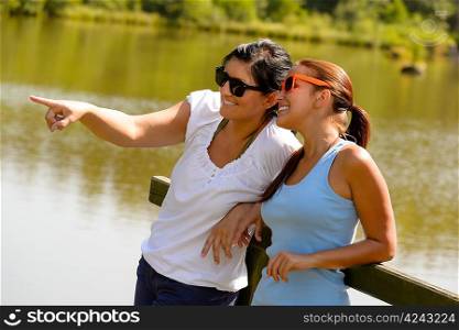Daughter and mother relaxing on lake pier happy teen pointing