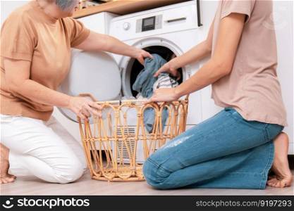 Daughter and mother working together to complete their household chores near the washing machine in a happy and contented manner. Mother and daughter doing the usual tasks in the house.. Contented daughter and mother in the household washing room working together.