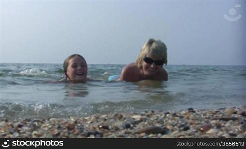 daughter and mum lay joyful in sea water.
