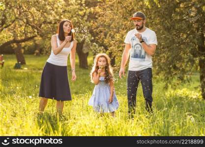 daughter blowing dandelion with her parents