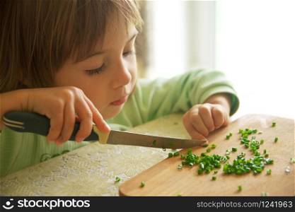 Daughter cutting green onion with knife. Food preparing and cooking scene.