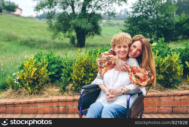 Daughter embracng her senior mother in wheelchair in the garden. Daughter embracing her senior mother in wheelchair