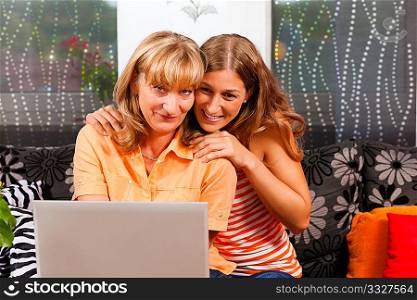 Daughter explaining internet to her mother at home, both women are sitting in front of a laptop PC