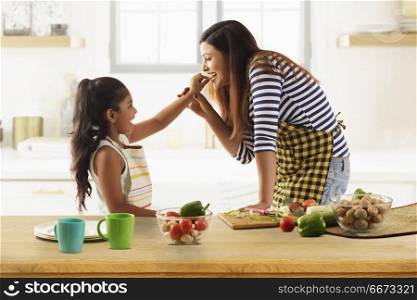 Daughter feeding cucumber to her mother in kitchen