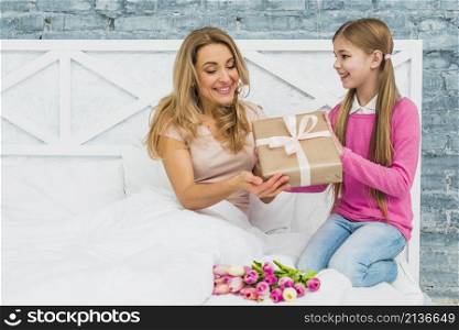 daughter giving gift box mother bed