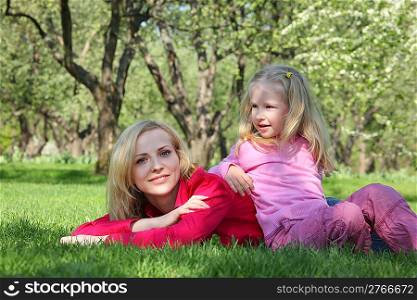 daughter has leant elbows on mother lying on grass in park