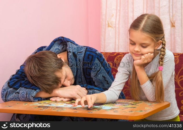 Daughter having fun collecting picture of puzzles while dad sleeps next