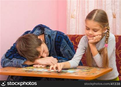 Daughter having fun collecting picture of puzzles while dad sleeps next