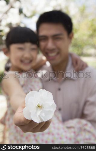 Daughter holding a cherry blossom close to the camera with her father in the park in springtime