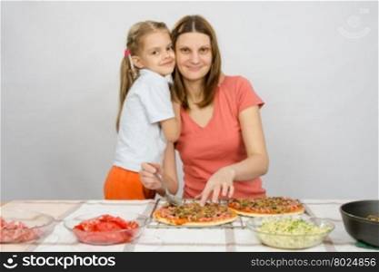 Daughter hugging her mother, which makes pizza at the table
