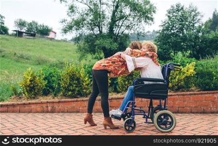 Daughter hugging her senior mother in wheelchair in the garden. Daughter hugging her senior mother in wheelchair