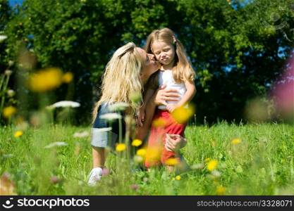 Daughter kissing and hugging her mother, both standing in the grass