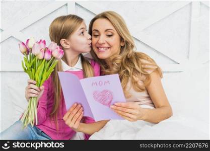 daughter kissing mother with greeting card