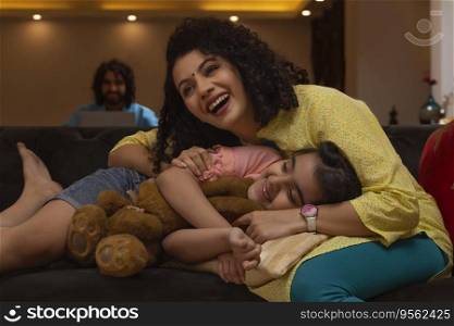 Daughter lying on her mother lap on sofa and father watching them from a distance