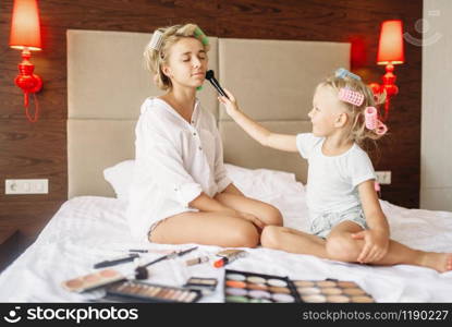 Daughter makes a funny makeup to her mother in bedroom at home. Parent feeling, togetherness, happy times