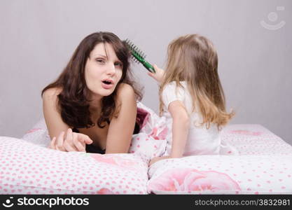 Daughter mother combing her hair lying in bed