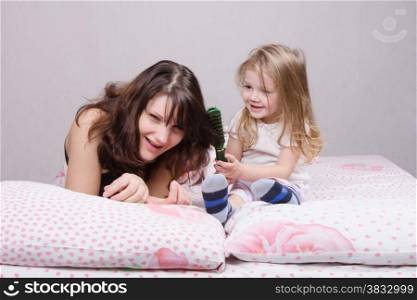 Daughter mother combing her hair lying in bed