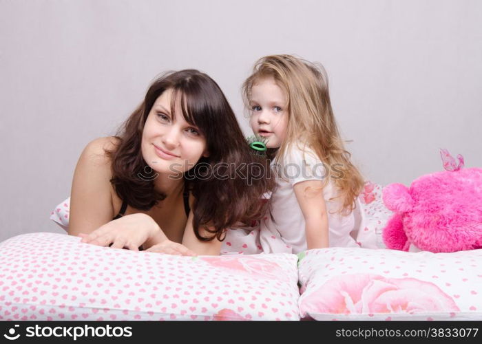 Daughter mother combing her hair lying in bed