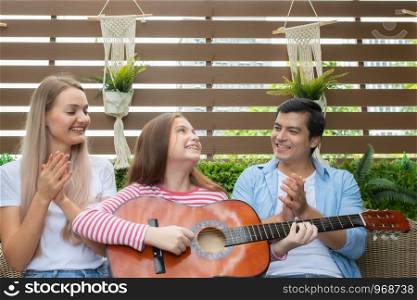 daughter play guitar and sing a song, father and mother sitting on sofa on garden home, mom and dad happy young family concept