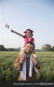 Daughter sitting on father&rsquo;s shoulders with the Indian flag in an agricultural field