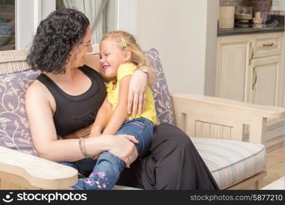 Daughter sitting on mother&rsquo;s lap outside on the porch of their house, having fun.