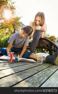 Daughter sitting on wooden decking drawing with mother