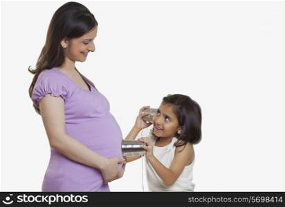 Daughter using tin can telephone on pregnant mother&rsquo;s belly