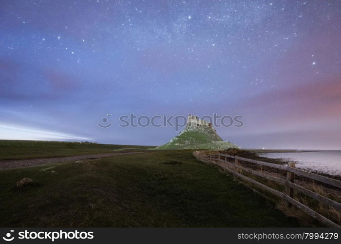 Dawn breaks over Lindisfarne Castle on Holy Island Northumberland with the stars and Milky Way still overhead in the fading night sky.