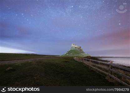 Dawn breaks over Lindisfarne Castle on Holy Island Northumberland with the stars and Milky Way still overhead in the fading night sky.