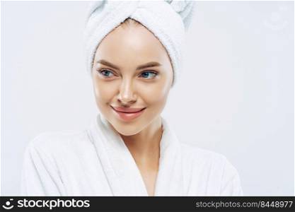 Day spa, beauty and freshness concept. Pensive European woman with healthy skin concentrated aside thoughtfully, feels refreshed after bath procedures, dressed in dressing gown, towel on head