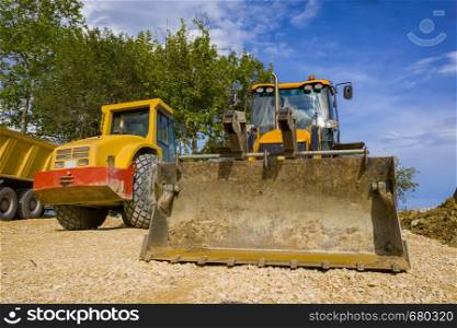 day view of yellow excavator with a shovel and single drum roller at the construction site