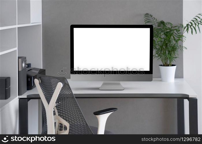 Daylight interior with white modern mock-up computer monitor on an office table, orthopaedic chair, and greenery pot on a desk, copy space. Concept of home remotely working.. Modern office working space with mock up computer screen.