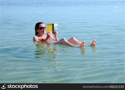 DEAD SEA, ISRAEL - NOVEMBER 19, 2010: Caucasian woman reads a book floating in the waters of the Dead Sea
