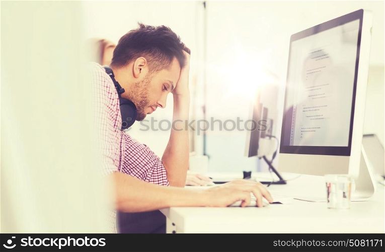 deadline, startup, education, technology and people concept - sad stressed software developer or student with headphones and computer at office. stressed software developer at office
