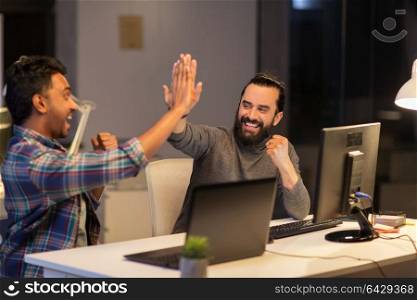 deadline, teamwork and success concept - creative team with computers making high five at night office. creative team making high five at night office