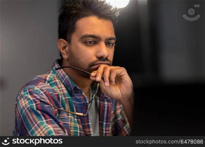 deadline, technology and people concept - close up of creative man with glasses working at night office and thinking. close up of creative man working at night office. close up of creative man working at night office