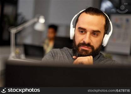 deadline, technology and people concept - creative man with headphones and computer listening to music and working at night office. creative man with headphones working at office. creative man with headphones working at office