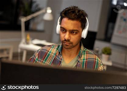 deadline, technology and people concept - creative man with headphones and computer listening to music and working at night office. creative man with headphones working at office