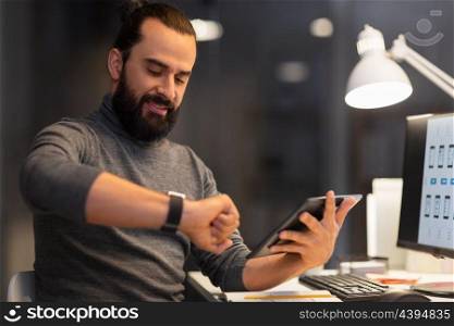 deadline, technology and people concept - creative man with smartwatch and tablet pc computer working late at night office. man with smartwatch and tablet pc at night office. man with smartwatch and tablet pc at night office