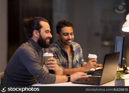 deadline, technology and people concept - creative team drinking coffee and working with computers late at night office. creative team drinking coffee at night office