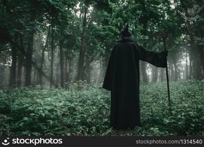 Death in a black hoodie and with a scythe in forest. Horror style, fear, spooky evil. Death in a black hoodie with a scythe in forest