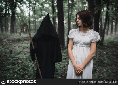 Death in a black hoodie swinging a scythe on young female victim, forest on background. Photo in horror style, mystery ritual. Death swinging a scythe on young female victim