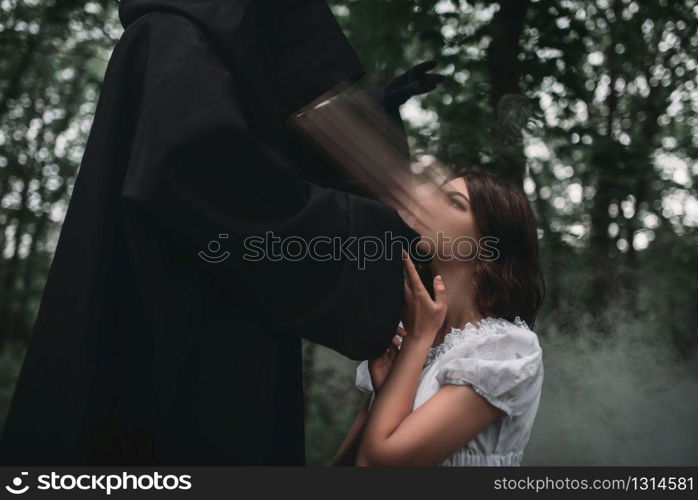 Death in a black hoodie takes the soul of young female victim, forest on background. Photo in horror style, mystery ritual. Death takes the soul of young female victim