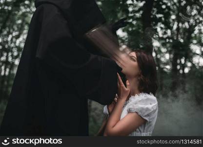Death in a black hoodie takes the soul of young female victim, forest on background. Photo in horror style, mystery ritual. Death takes the soul of young female victim