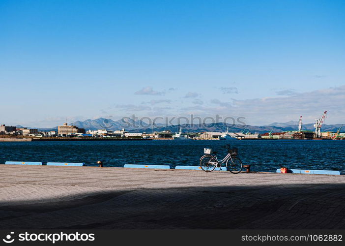 DEC 1, 2018 Hakkodate, Japan - Hakkodate port pier with bicycle in bright winter sun blue sea cityscape in background.