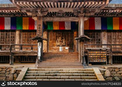 DEC 3, 2018 Yamagata, Japan - Japanese carved wood smiling Buddha statue with old wood wall and colourful flag of Konponchudo main hall in Yamadera Risshaku ji temple