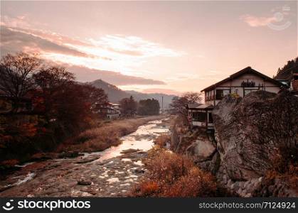 DEC 3, 2018 Yamagata, Japan - Old Japanese house on rock cliff by Tachiya river with evening sunset light and warm tone sky in late autumn