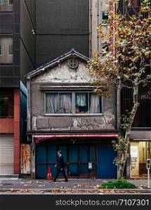 DEC 5, 2018 Tokyo, Japan - Old small Japanese house among modern buildings in Kanda business district near Tokyo city center with local business man walking on sidewalk - Conflict between old world and new wolrd concept